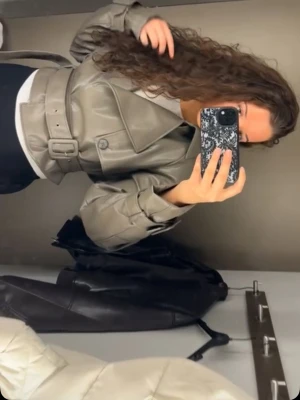 Grå skinnjacka med bälte - Säljer min super snygga skinjacka i militärgrönaktig färg. Har ett snyggt bälte man kan justera i midjan och även spännen i ärmarna! Endast använd en gång😎