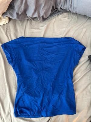 Blå topp med öppen rygg  - En stilren kornblå topp med korta ärmar, öppen rygg och rund halsringning. Modellen är rak och enkel, perfekt att matcha med jeans eller kjol. Tunt och mjukt material som känns skönt mot huden. 