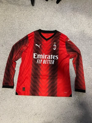 AC Milan långärmad matchtröja Puma - Säljer en långärmad AC Milan matchtröja från Puma i rött och svart med coolt grafiskt mönster. Tröjan har klubbmärke, Puma-logga och sponsortryck på bröstet samt svart V-ringning. Tillverkad i lätt och ventilerande material, perfekt för fotboll eller träning.