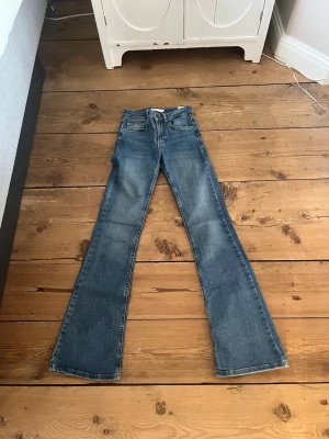 Blå bootcut jeans med utsvängda ben - Ett par klassiska blå bootcut jeans med utsvängda ben och femficksmodell. Jeansen har normalhög midja och är tillverkade i denim. Perfekta för en avslappnad och trendig look.