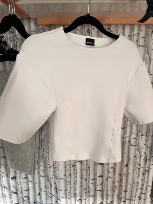 Vit croppad topp från Gina Tricot - Säljer en stilren vit croppad topp från Gina Tricot. Toppen har korta ärmar, rund halsringning och markerade sömmar framtill för en modern look. Funkar perfekt till ett par bootcut eller baggy jeans! Den är oanvänd då jag upplevde den snäppet för liten för mig!