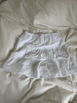 Vit volangkjol i bomull - Söt vit kortkjol med volangdetaljer och resår i midjan. Kjolen är gjord i lätt bomullstyg och har en luftig känsla, perfekt för varma dagar. Enkel att matcha med olika toppar. Kortare än den ser ut, mer av en minikjol. Den har inga fläckar eller nått utan kommer bara inte till användning. 