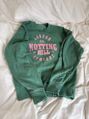 Grön sweatshirt Notting Hill Company - Cool grön sweatshirt med rosa tryck 'London The Notting Hill Company 2023' på bröstet. Tröjan har rund hals, ribbade muddar och är mjukt material. Använd 1 gång men sen har jag glömt bort den. Köpt i London. Fett bra passform. 