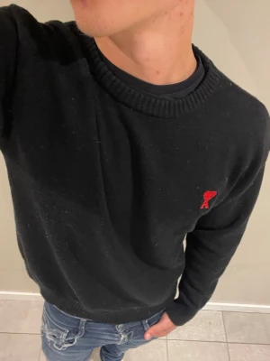 Svart stickad tröja från Ami Paris - Svart stickad tröja från Ami Paris med rund halsringning och ribbade muddar. Tröjan har Ami Paris klassiska röda hjärtemblem broderat på bröstet. Perfekt till jeans och enkel att matcha med andra plagg. 💋Modellen bär storlek M och är 181 cm lång och väger 76 kg kom gärna vid frågor eller funderingar💋