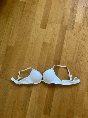 Vit push-up bh från Lindex - Snygg vit push-up bh från Lindex med vadderade kupor och justerbara axelband. Klassisk modell med hakknäppning bak och slät yta som passar under de flesta plagg. Perfekt för dig som vill ha extra stöd och lyft. 