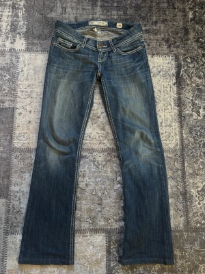 Vintage blå jeans  - Säljer ett par blå jeans  med slitna detaljer och kontrastsömmar. Jeansen har låg midja och bakfickor med broderade kanter. Köpt vintage i stockholm. 