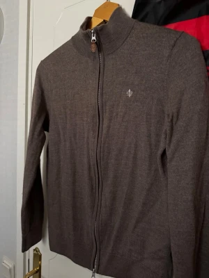 Morris zip kofta - Snygg brun ziptröja med hög krage och diskret broderad detalj på bröstet. Tröjan har långa ärmar, ribbade muddar och är tillverkad i ett tunt, mjukt material som passar perfekt till lager på lager. Enkel och stilren design. Sparsamt använd inga hål, djur o rökfritt hem