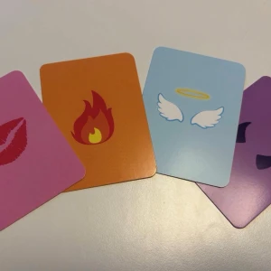 Sällskapsspel för ungdomar  - Ett roligt och färgglatt frågespel med kort i rosa, orange, blå och lila, dekorerade med olika emojis som eld, kyss, änglavingar och djävulshorn. Perfekt för att lära känna vänner bättre och skapa skratt under spelkvällen.