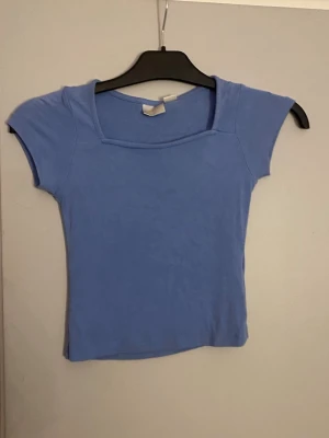 Blå croppad topp med kort ärm - Snygg ljusblå croppad topp med korta ärmar och fyrkantig halsringning. Perfekt för dig som gillar en enkel och stilren look. Materialet känns mjukt och stretchigt, vilket gör den bekväm att bära hela dagen.