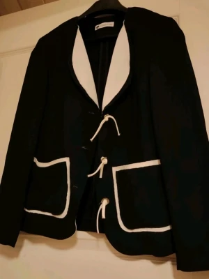Vintage❤️ Svart kavaj med vita detaljer💎  - Stilren svart kavaj från Merrytime med vita kontrastdetaljer längs krage och fickor😍 Kavajen har unika knytningar framtill istället för vanliga knappar och två stora fickor. Perfekt för dig som vill sticka ut med en cool och modern look🖤🤍 S-M. 