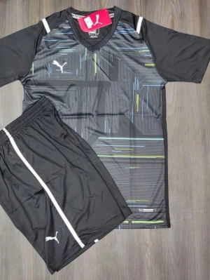 Svart träningsset från Puma - Snyggt svart träningsset från Puma med t-shirt och shorts. T-shirten har grafiskt mönster i blått, grönt och vitt samt vita detaljer på axlarna. Shortsen är svarta med vit rand och Puma-logga. Perfekt för träning eller sportaktiviteter.