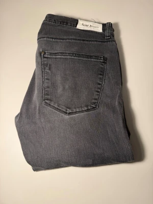 Grå jeans från Acne Studios - Snygga grå jeans från Acne Studios med klassisk femficksmodell och raka ben. Jeansen har silverfärgade nitar och knapp, samt Acne Jeans-märke i midjan. Tillverkade i mjukt denimtyg som ger en avslappnad look. Står 33/33 men passar mig 31/32