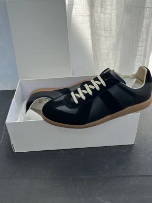Maison Margiela sneakers – svarta - Kvitto finns! Säljer ett par stilrena och ikoniska Maison Margiela sneakers i storlek 43. Klassisk modell, här i en snygg svarta färgkombination med mocka och läder samt beige gummisula. Pris kan diskuteras! Skickar inom 12h av köpet!