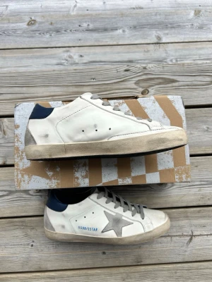 Vita Golden Goose sneakers 40 - De är allmänt sköna. Man kan gå med de till skolan samt jobb. Men även är de snygga så man kan gå på restaurang o annat fint. Haft dessa i nån månad men inte använt de hela tiden. Perfekta nu inför sommaren om man vill hålla en skön look. Använde dessa första gången jag träffa min tjej. Så de e en brudmagnet😉                                               Skick 6-7/10 använt sparsamt, ända defketen är hälen(5)✅ Skorna kommer med boxen samt GGDB påsen📦Nypris på dessa ligger på runt 6000🤑storlek 40