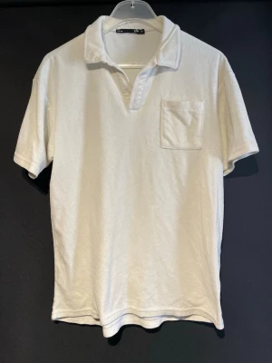 Vit frotté t-shirt med krage - Säljer en vit t-shirt i mjuk frotté med klassisk krage och bröstficka. T-shirten har korta ärmar och en relaxed passform som ger en chill vibe. Perfekt för dig som gillar stilrena plagg med en twist. Det är M men sitter mer som L.