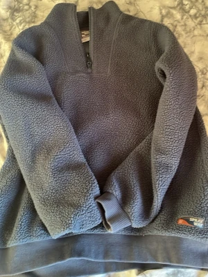 Blå fleece-tröja från Sprayway - Mysig blå fleece-tröja från Sprayway med halv dragkedja framtill och ribbade muddar. Perfekt för kyliga dagar och outdoor-aktiviteter. Tröjan har en klassisk passform och är tillverkad i mjukt fleecematerial.