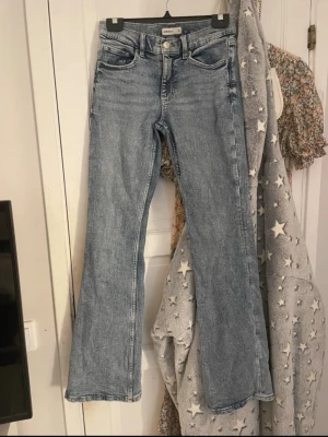 Blå bootcut jeans från Gina tricot  - Snygga ljusblå bootcut jeans från Gina tricot i klassisk tvättad denim. Jeansen har fem fickor, medel midja och utsvängda ben. Perfekta för en avslappnad och trendig look. Passar till det mesta och är ett måste i garderoben!