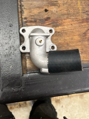 Metallrör med gummimanschett - Säljer ett böjt metallrör med fläns och fyra monteringshål, samt en svart gummimanschett på ena änden. Perfekt för dig som behöver reservdel till maskin eller motor. Materialet är metall och gummi, färgen är silver och svart.