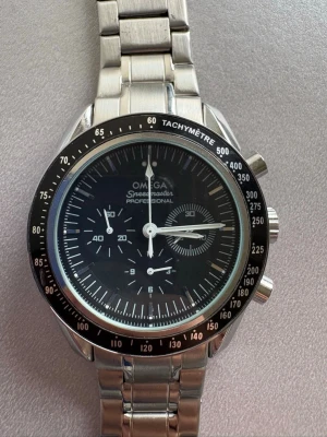 Omega Moonwatch  klocka - Säljer en klassisk Omega Speedmaster Professional med svart urtavla, tachymeter-ram och länkarmband i silverfärgat stål. Klockan har kronograf och flera subdials. Extra länkar medföljer så du kan justera storleken enkelt.