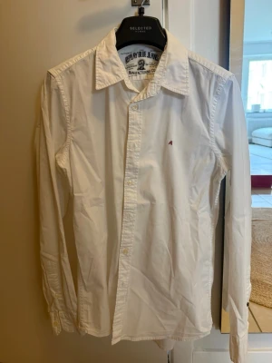 Vit skjorta från Replay - Klassisk vit skjorta från Replay med diskret broderad logga på bröstet. Skjortan har lång ärm, knappar framtill och en tidlös krage. Tillverkad i bomull för en skön och luftig känsla.