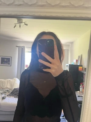 Svart mesh polotopp - Säljer en svart mesh polotopp med lång ärm och tight passform. Toppen är genomskinlig och har en hög hals.