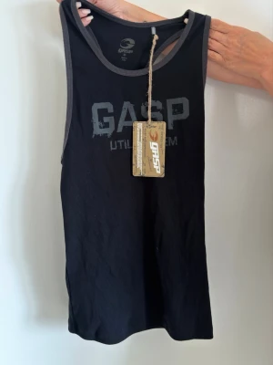 Svart linnetopp från GASP - Snygg svart linnetopp från GASP med grå kantband och tryckt logga framtill. Modellen är ärmlös och har en sportig design med brottarrygg, perfekt för gymmet eller träning. Tillverkad i mjuk bomull för skön känsla.