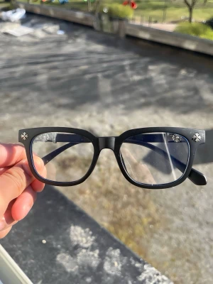 Chrome heart style glasses  - Snygga svarta solglasögon med markerad båge och unika silverfärgade korsdetaljer på skalmarna. Glasögonen har en klassisk fyrkantig form och passar perfekt för dig som vill sticka ut lite extra.