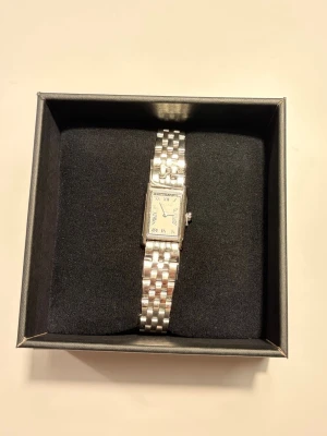 Silverfärgad dam klocka Carrie Taylor - Stilren klocka från Carrie Taylor New York med silverfärgad länkarmband och rektangulär urtavla. Urtavlan har romerska siffror och klassisk design. Perfekt accessoar för dig som gillar en tidlös och elegant look. Klockan är sprillans ny och har ej använts, säljer pga att jag fick det som present men har redan en liknande klocka! Ordinariepris: 1599kr!