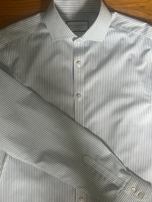 Randig skjorta från Charles Tyrwhitt - Snygg randig skjorta från Charles Tyrwhitt i extra slim fit. Skjortan är ljusblå och vit med klassisk krage och knäppning framtill. Tillverkad i bomull och är non-iron, vilket gör den enkel att sköta. Perfekt för en stilren look.