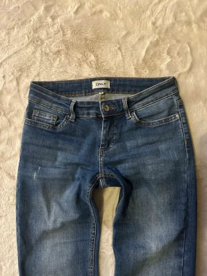 Blå lågmidjade bootcut jeans från ONLY  - Säljer ett par blå lågmidjade bootcut jeans från ONLY. Jeansen har en snygg tvätt och utsvängda ben. Perfekta till en avslappnad stil och funkar året runt. Materialet är stretchigt för extra komfort.