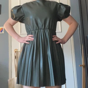 Grön kort klänning med puffärm - Snygg grön kort klänning i syntetmaterial med puffärmar och plisserad kjol. Klänningen har rund halsringning och en loose passform som ger en cool och trendig look. Perfekt för dig som vill sticka ut lite extra. Klänningen är köpt på Zara och jag fick den av min mammas vän när jag var yngre, så jag vet nt hur den här tagits hand av dem. Modellen går inte att köpa längre och andra bilden är från Sellpy. ✨✨