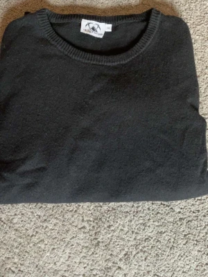 Svart stickad tröja Stiggruvan - Klassisk svart stickad tröja från Stiggruvan med rund halsringning och ribbade muddar. Perfekt basplagg som funkar till det mesta och är enkel att matcha. Tröjan är i mjukt material och har en stilren look.