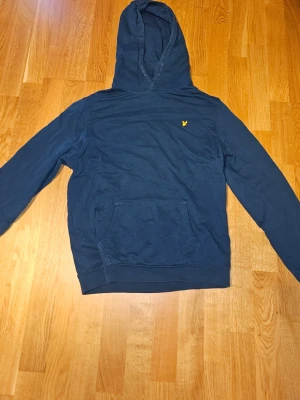 Lyle & Scott Hoodie - Snygg mörkblå hoodie från Lyle & Scott med klassisk huva och känguruficka framtill. Strl 15-16 år. Fint skick!