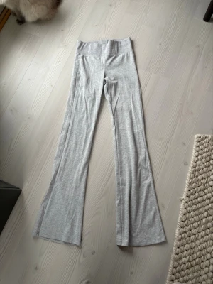 Grå ribbade bootcut leggings från stravadius. - Snygga ljusgrå leggings med ribbad struktur och utsvängda ben. Hög midja för en bekväm passform och trendig siluett. Perfekta att matcha med en crop top eller oversized hoodie. Materialet känns mjukt och stretchigt.