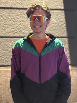 Retro vindjacka i lila och svart - Säljer en retro vindjacka med färgblock i lila, svart och grönt. Jackan har dragkedja framtill, hög krage och klassisk 90-talslook. Perfekt för dig som gillar vintage och streetwear. Materialet är tunt och lätt, typiskt för vindjackor.