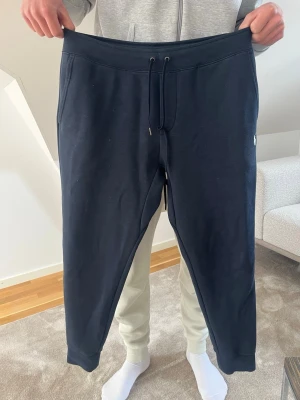 Marinblå mjukisbyxor Polo Ralph Lauren - Snygga marinblå mjukisbyxor från Polo Ralph Lauren med dragsko i midjan och ribbade muddar vid bensluten. Tillverkade i mjukt bomullsmaterial för maximal komfort. Perfekta för chill dagar eller när du vill ha en avslappnad stil.