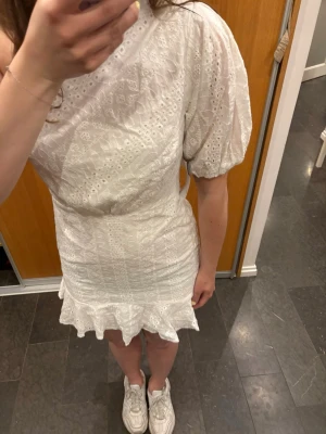 Vit one shoulder klänning  - Säljer en vit kortklänning med one shoulder och puffärm. Klänningen har broderade detaljer och volangkant nertill. Perfekt för sommarens alla tillfällen! 😊