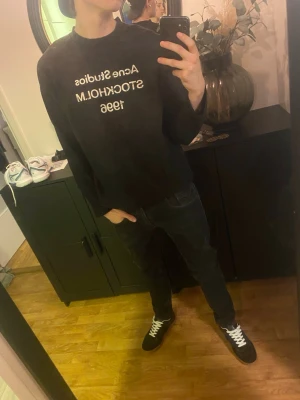 Svart långärmad t-shirt Acne Studios - Svart långärmad t-shirt från Acne Studios med vit text på bröstet där det står 'Acne Studios STOCKHOLM 1996'. Klassisk passform och rund halsringning. Perfekt för dig som gillar stilrena och trendiga plagg.