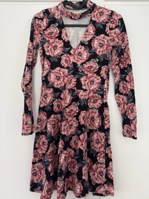 Blommig långärmad klänning Hollister - Supersnygg blommig klänning från Hollister med rosa och vinröda blommor på svart botten. Klänningen har lång ärm, v-ringning och en lätt utställd kjol. Perfekt för dig som vill sticka ut med ett färgstarkt mönster.