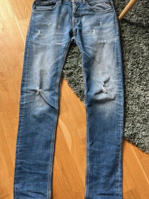 Blåa Replay jeans  - Säljer ett par Replay jeans med slitningar och en skön tvätt. Byxorna är i regular slim fit. Man kan säga att de mellan straight och tapred. Riktigt snygga och bra skick. Storlek 31/34