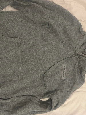 Grå hoodie från Peak Performance - Snygg grå hoodie från Peak Performance med klassisk logga på bröstet. Hoodien har huva med dragsko och en stor magficka framtill. Tillverkad i mjukt bomullsmaterial som känns skönt mot huden. Perfekt för en avslappnad och sportig stil.