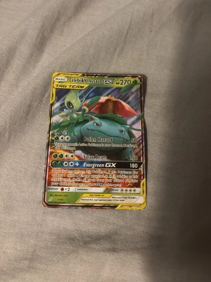 Pokémonkort Celebi & Venusaur GX - Säljer ett Pokémonkort med Celebi & Venusaur GX TAG TEAM. Kortet har färgstark design med gröna och röda toner, holografisk yta och detaljerade illustrationer. Perfekt för samlare eller Pokémonfans som vill utöka sin samling.