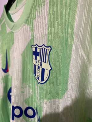 Grön FC Barcelona matchtröja Nike Lamine yamal 19 - Snygg grön FC Barcelona matchtröja från Nike med klubbmärke och sponsorlogga från Spotify på bröstet. Tröjan har korta ärmar, rund hals och ett unikt mönster i olika gröna nyanser. Lamine yamal 19. Storlek L (denna finns inne hos oss nu)