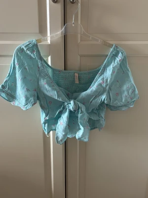 Blommig blå omlottopp med knyt från Y.A.S. - Supersöt ljusblå topp med små blommor i rosa och vitt. Modellen har korta puffärmar, v-ringning och knyt framtill. Materialet känns lätt och luftigt. Sitter snyggt croppad och har en romantisk vibe. Aldrig använd. Storlek M. Från Y.A.S.