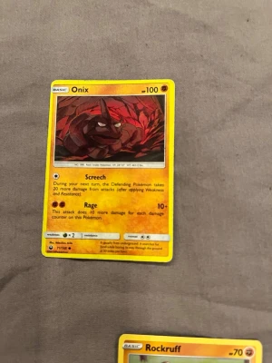 Onix Pokémonkort - Säljer ett Onix Pokémonkort med gul ram och färgstark illustration av Onix i rödbruna toner. Kortet har attackerna Screech och Rage, samt HP 100. Perfekt för dig som samlar eller spelar Pokémon TCG.