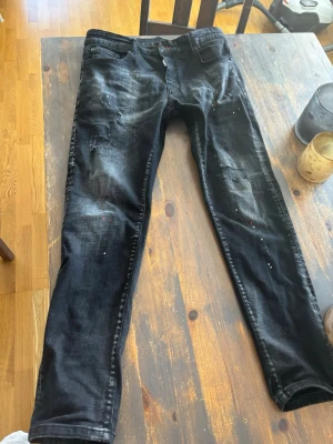 Svarta distressed jeans från Dsquared2 - Coola svarta jeans från Dsquared2 med slitningar, färgstänk och distressed detaljer. Skinny fit och klassisk femficksdesign. Jeansens material är denim och de har en modern, trendig look som passar perfekt till streetstyle.