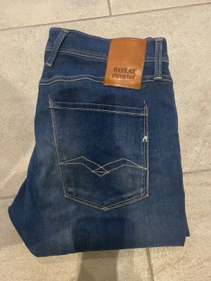 Blå Replay Hyperflex jeans - Snygga blå jeans från Replay Hyperflex med klassisk femficksmodell och kontrastsömmar. Jeansen har en skinnpatch med logga bak i midjan och diskret sliten tvätt för en modern look. Materialet är stretchigt för extra komfort 31/32.
