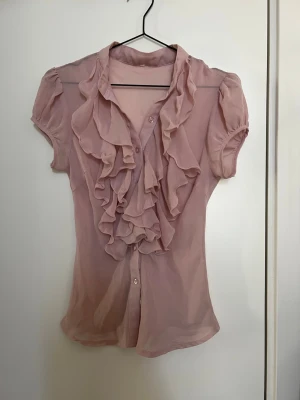 Ljusrosa blus med volanger - Rosa mesh blus köpt på Plick, den har inte kommit till användning.