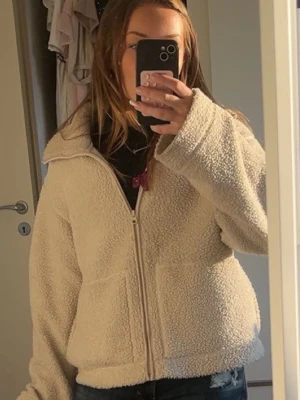 Beige teddyjacka med dragkedja - Mysig beige teddyjacka med dragkedja framtill och två stora fickor. Jackan har en bred krage och är gjord i fluffigt teddy-material som ger en avslappnad och trendig look. Perfekt för att hålla värmen under kyliga dagar.andvönd mycket med små fläckar(skorv för bilder) storlek M🥰