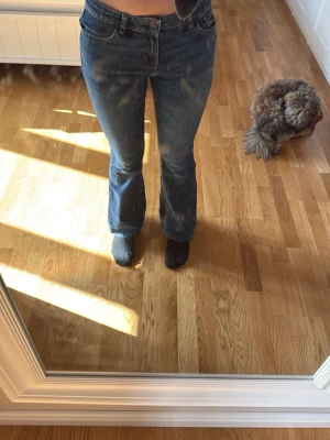 Blå bootcut jeans med slitningar - Säljer ett par blå bootcut jeans med snygga slitningar och klassisk femficksmodell. Jeansen har normal midja och är tillverkade i ett mjukt denimtyg som sitter skönt. Perfekta för dig som gillar en avslappnad men trendig look.